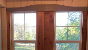 A dining area with a wooden table and chairs, large windows with a view of a grassy yard.