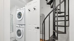 Une buanderie équipée d’un lave-linge et d’un sèche-linge à chargement frontal, d’une porte blanche et d’un escalier en colimaçon en métal noir.