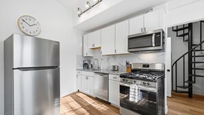 Une cuisine moderne dotée d’appareils électroménagers en acier inoxydable, de meubles blancs, d’un four à micro-ondes encastré et d’une cuisinière à gaz.