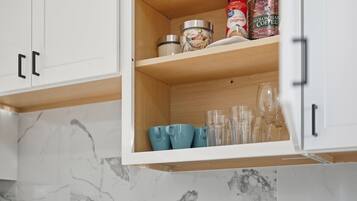 A kitchen cabinet with a marble backsplash, containing a coffee can, a jar, and several glassware items.