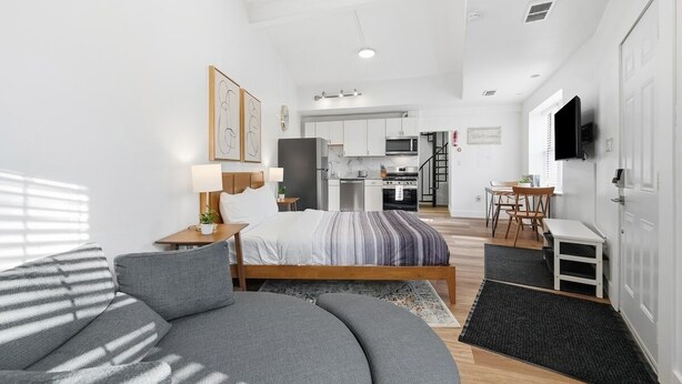 Une chambre moderne avec un grand lit, un canapé, un bureau et, au fond, un coin cuisine.