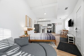 Une chambre moderne avec un grand lit, un canapé, un bureau et, au fond, un coin cuisine.