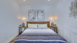 Un dormitorio con una cama grande, dos mesitas de noche con lámparas y dos obras de arte colgadas en la pared.