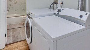 Un cuarto de lavado con lavadora y secadora, zona de ducha y conducto de ventilación.