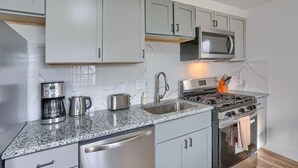 Una cocina moderna con gabinetes grises, un microondas de acero inoxidable, una estufa a gas y una cafetera.