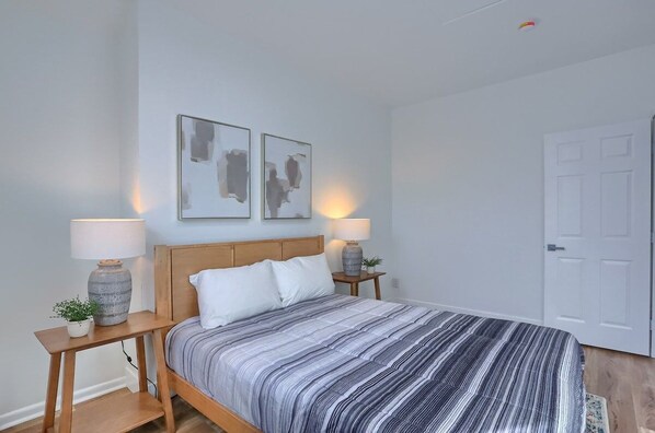 A bedroom with a bed, two bedside tables, two lamps, and two abstract wall art pieces. - Spacious and Modern Three Bedroom Apartment in Pittsburgh, Free Street Parking (Pittsburgh)
