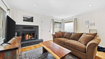 Una sala de estar con chimenea, un sofá marrón, una mesa de centro de madera y un televisor sobre un mueble de madera.