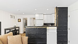 Uma cozinha moderna com armários brancos, uma parede de destaque em pedra preta e uma mesa de jantar de madeira com cadeiras.