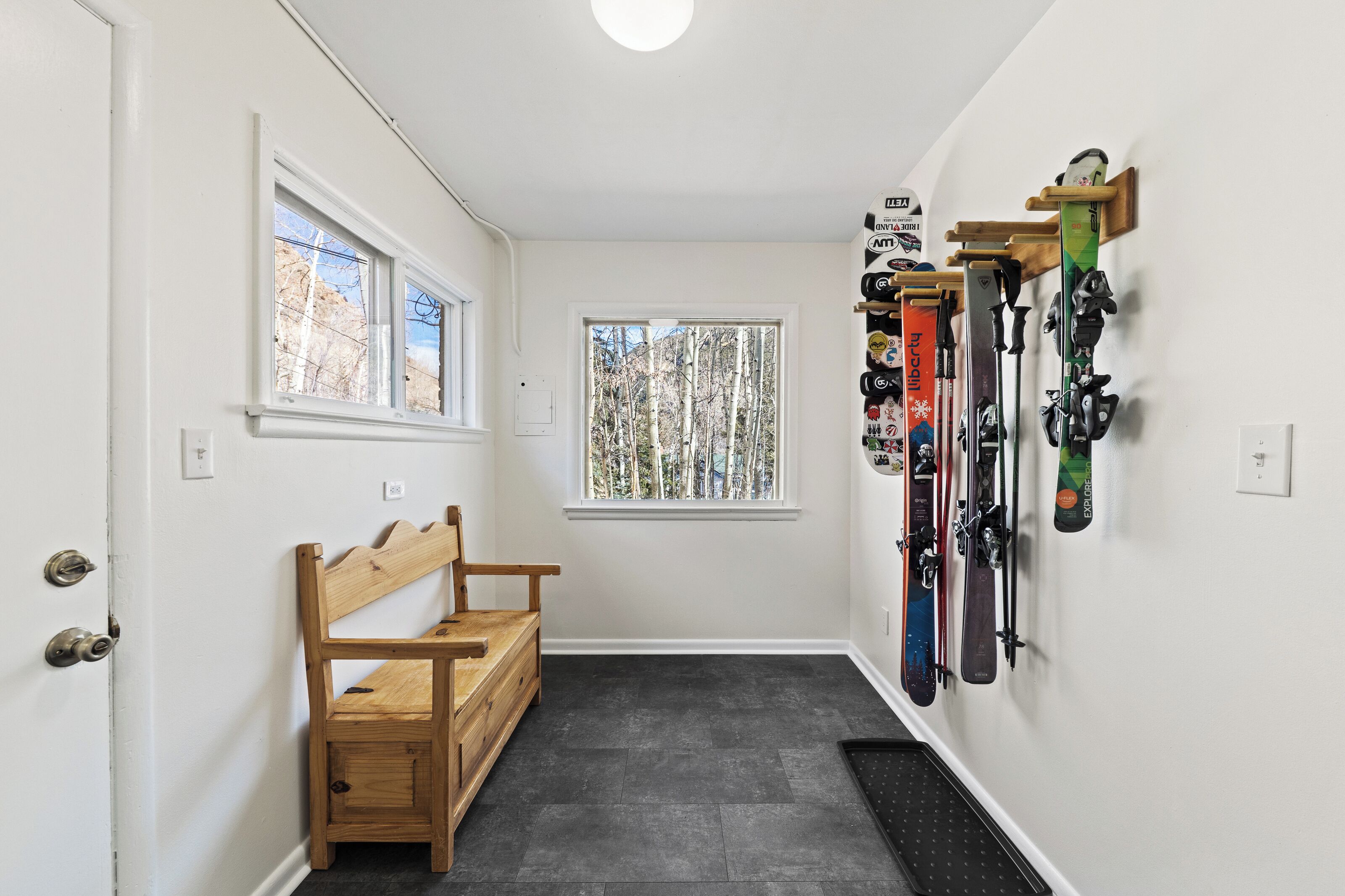 Un couloir avec un banc, une fenêtre et un porte-skis fixé au mur.