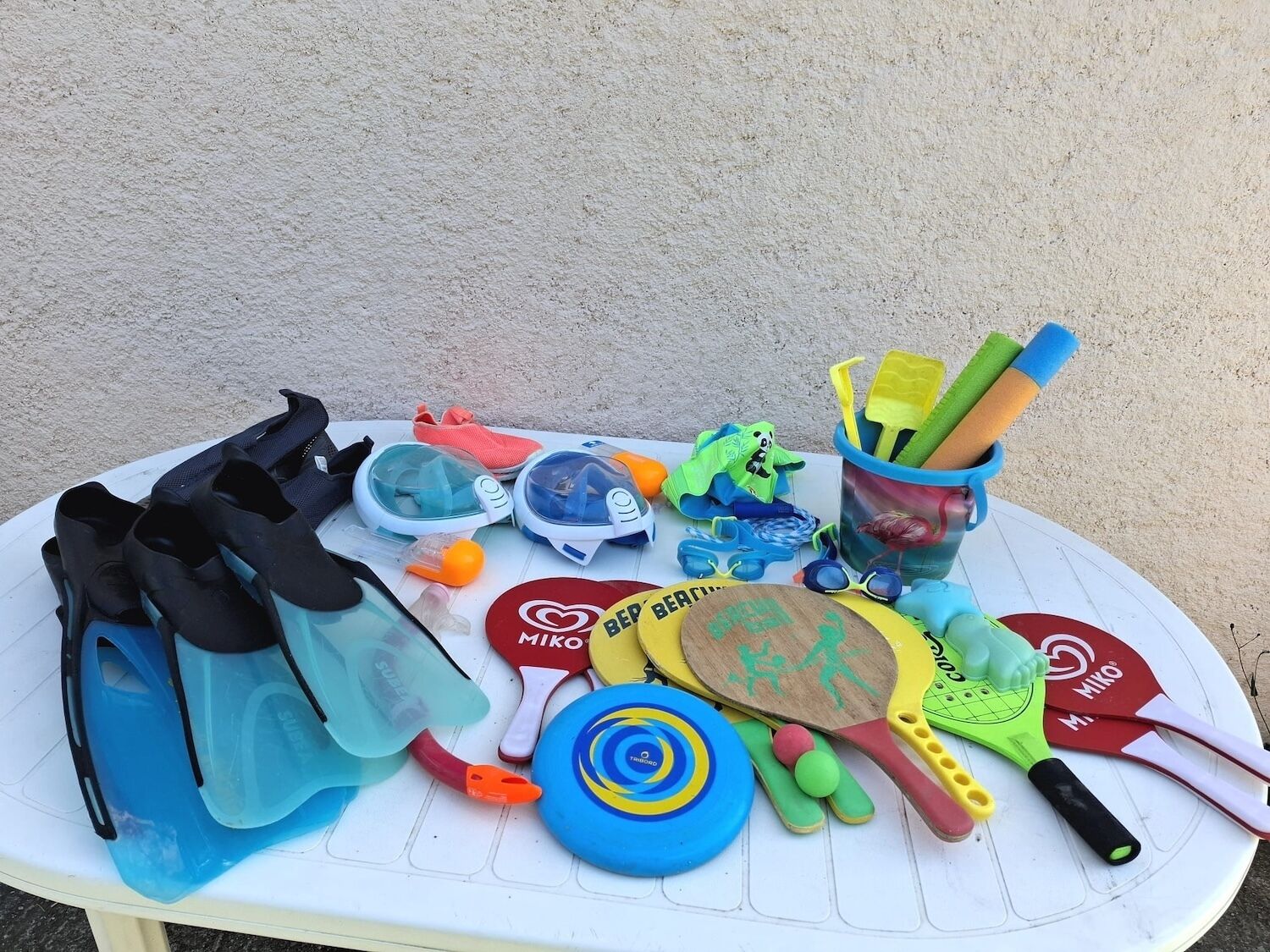A table with various beach toys and equipment, including a pair of swim fins, a pair of goggles, a beach ball, and a paddle.