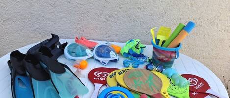 A table with various beach toys and equipment, including a pair of swim fins, a pair of goggles, a beach ball, and a paddle.