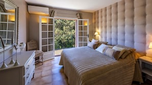 Un dormitorio con una cama grande, un aparador, un espejo y una ventana con vistas a la vegetación.