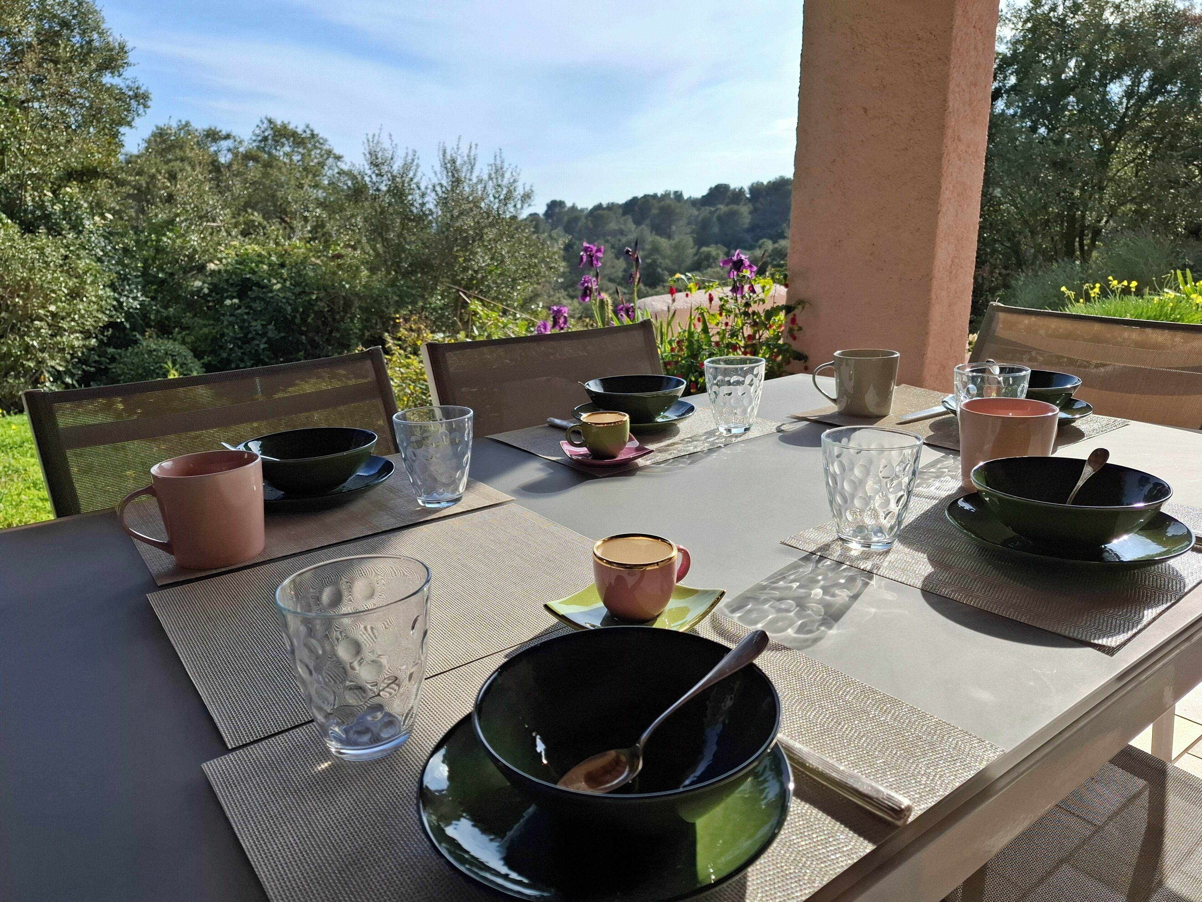 A dining table set outdoors with various bowls, glasses, and a pink mug.