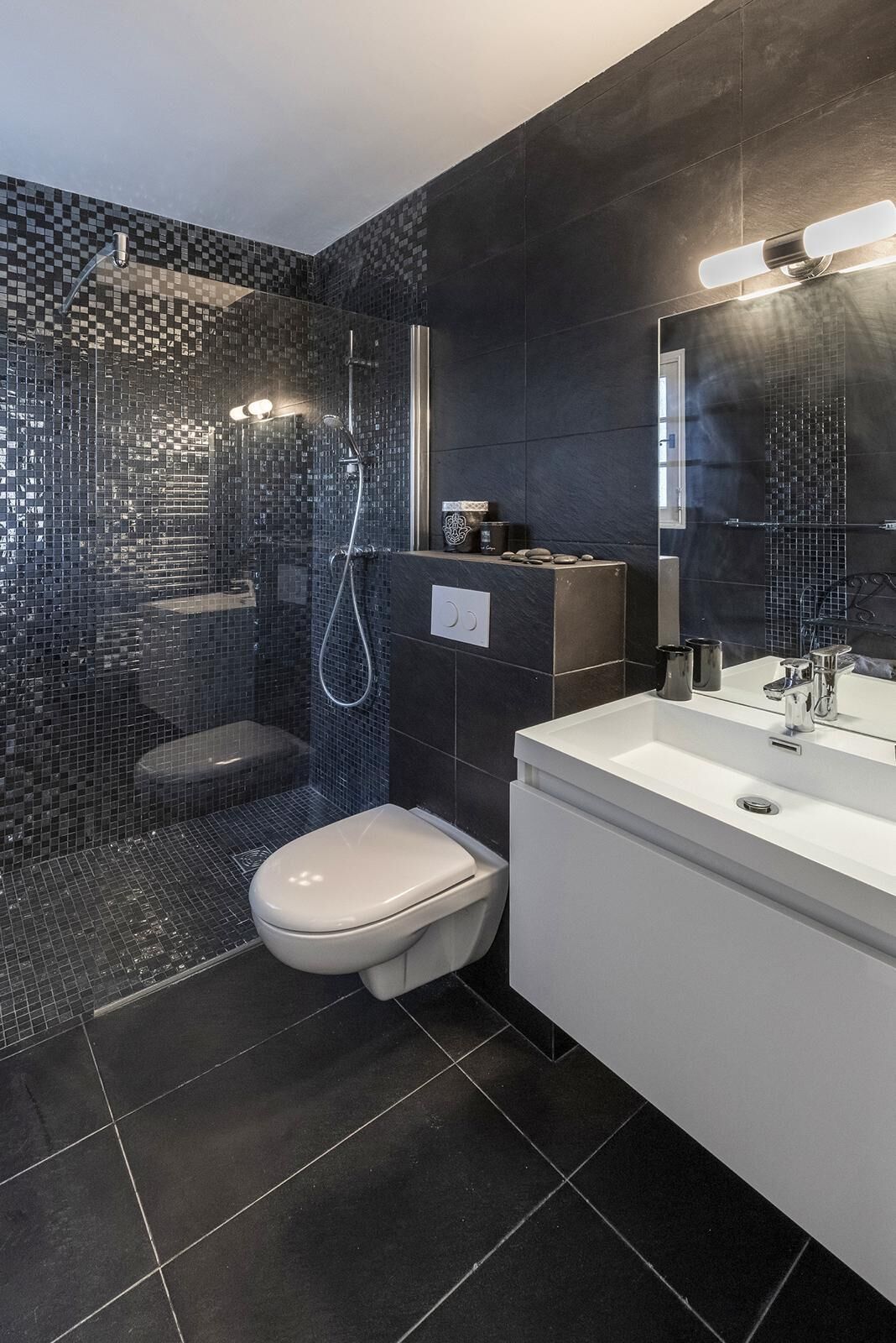 A modern bathroom with a mosaic shower wall, a toilet, and a white sink with a mirror.