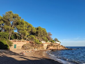 Uma praia com pessoas tomando sol, um muro de pedra e árvores.