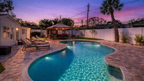 Una piscina de diseño curvo, rodeada por un patio de piedra y sillones de descanso.