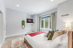 Ein Schlafzimmer mit Bett, einem an der Wand befestigten Fernseher, einem Fenster mit Vorhängen und einem Schild an der Wand.