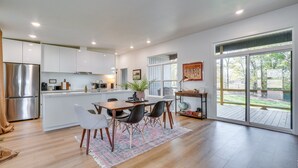 A modern kitchen with white cabinets, a stainless steel refrigerator, and a dining area with a table and chairs.