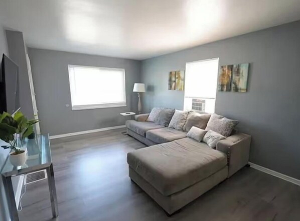A spacious living room with a large sectional sofa, a glass coffee table, and a potted plant. - Comfortable two bedroom with plenty of space for the family! (Dayton)