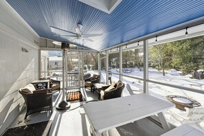 A covered outdoor seating area with a ceiling fan, a grill, and a view of a snowy backyard.