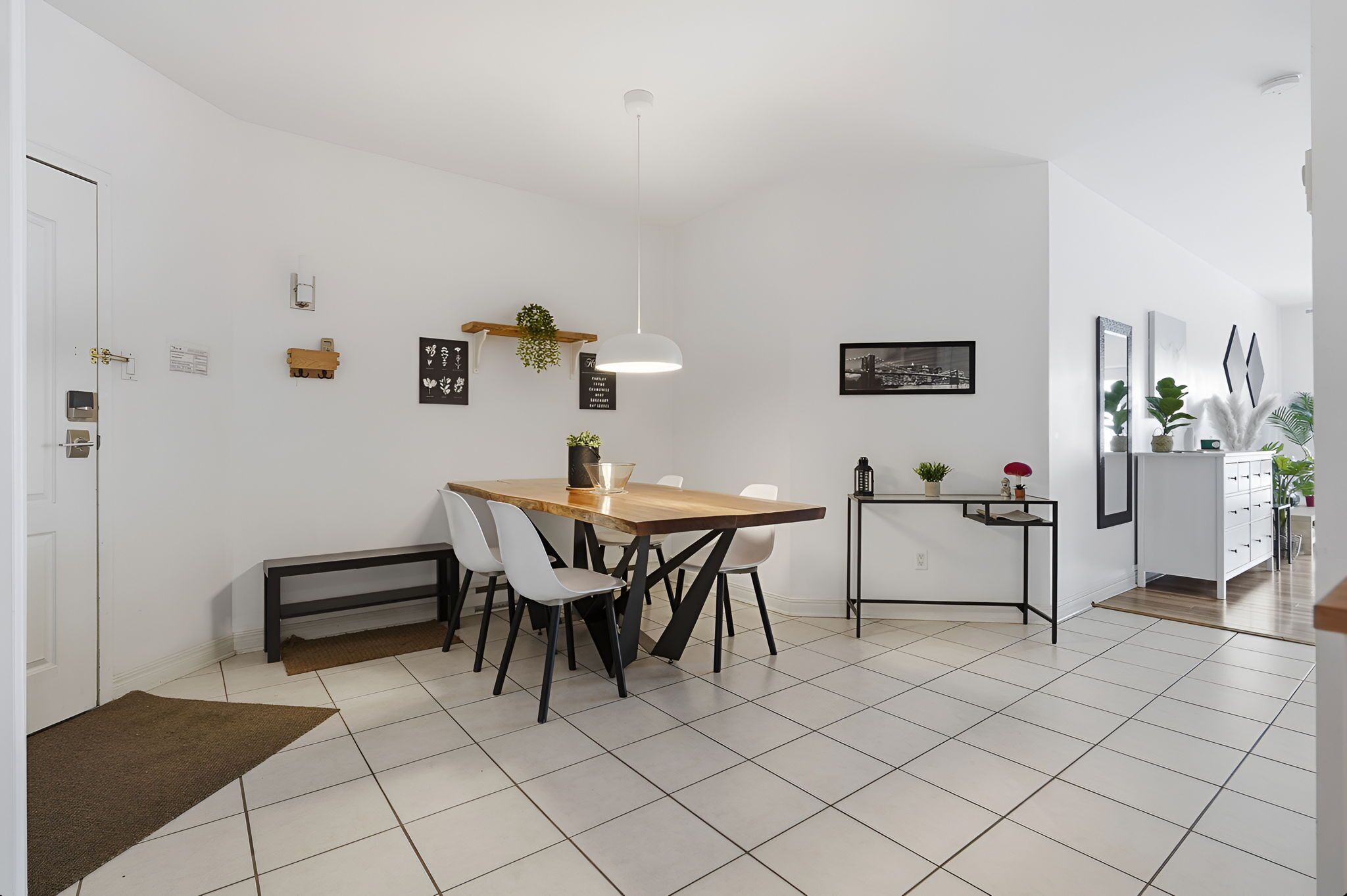 A modern kitchen with a dining table, chairs, a bench, and a hanging light fixture.