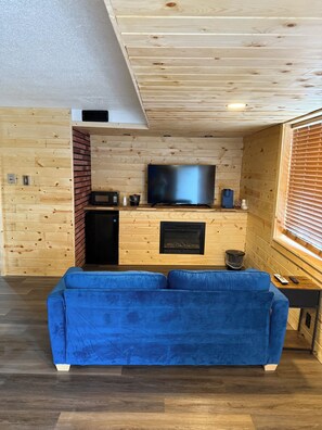 A cozy living room with a blue sofa, a flat-screen TV, a fireplace, and wooden walls. - Lake Lawn Inn (Pana)