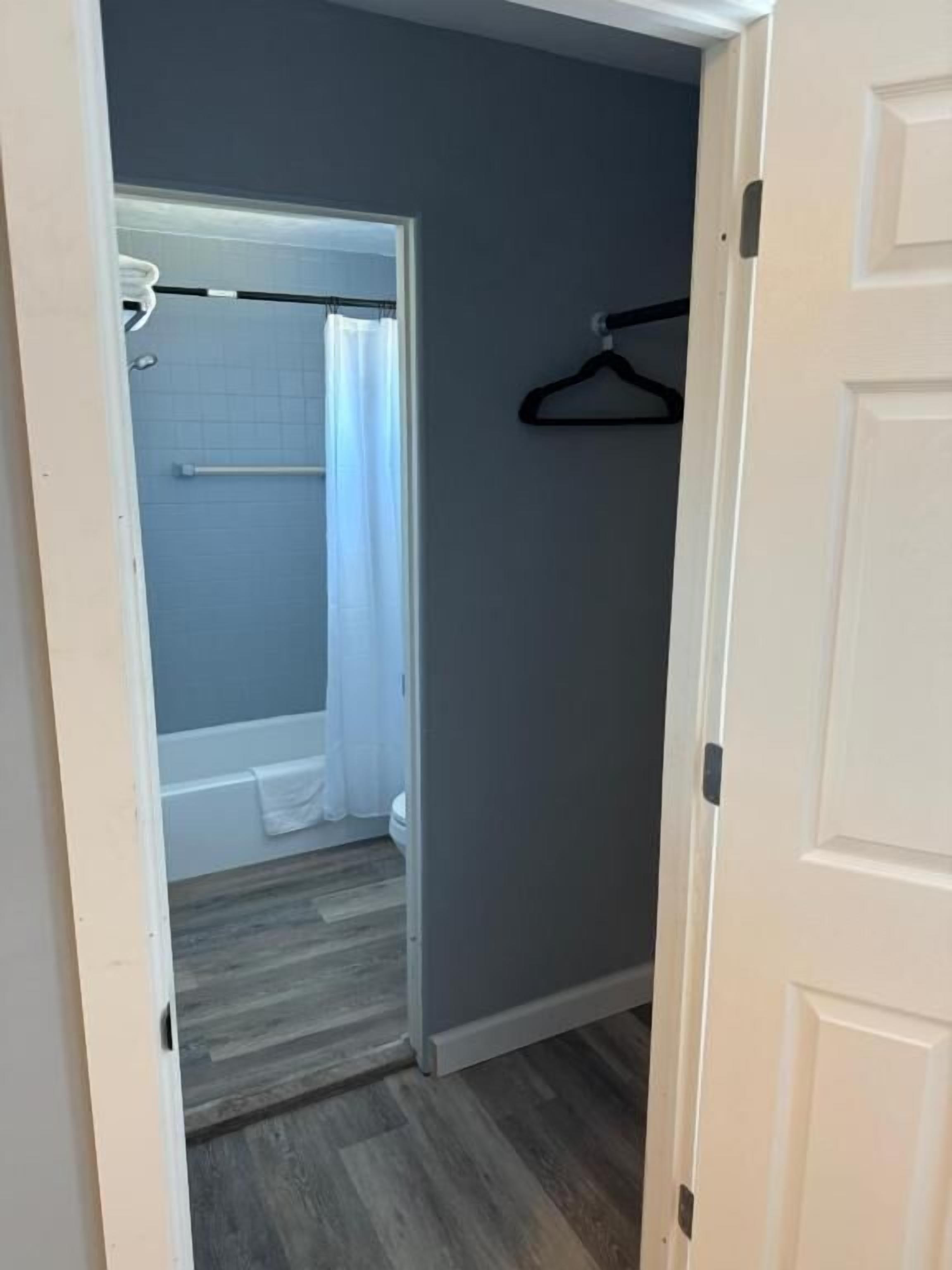 A narrow hallway with a door leading to a bathroom. The bathroom has a bathtub, a shower curtain, and a towel rack.