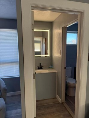 A compact bathroom with a mirror, sink, and toilet. - Lake Lawn Inn (Pana)