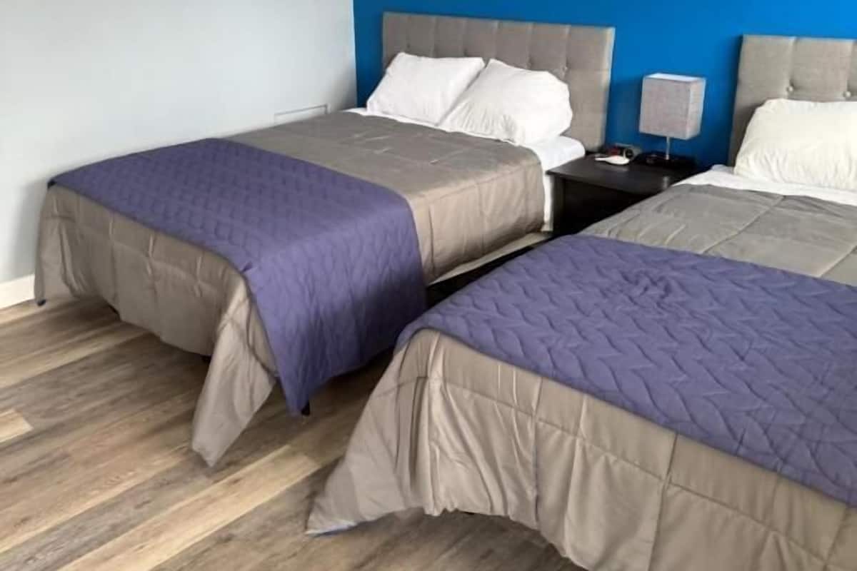 A hotel room with two beds, each with a headboard and footboard, and a nightstand between them.