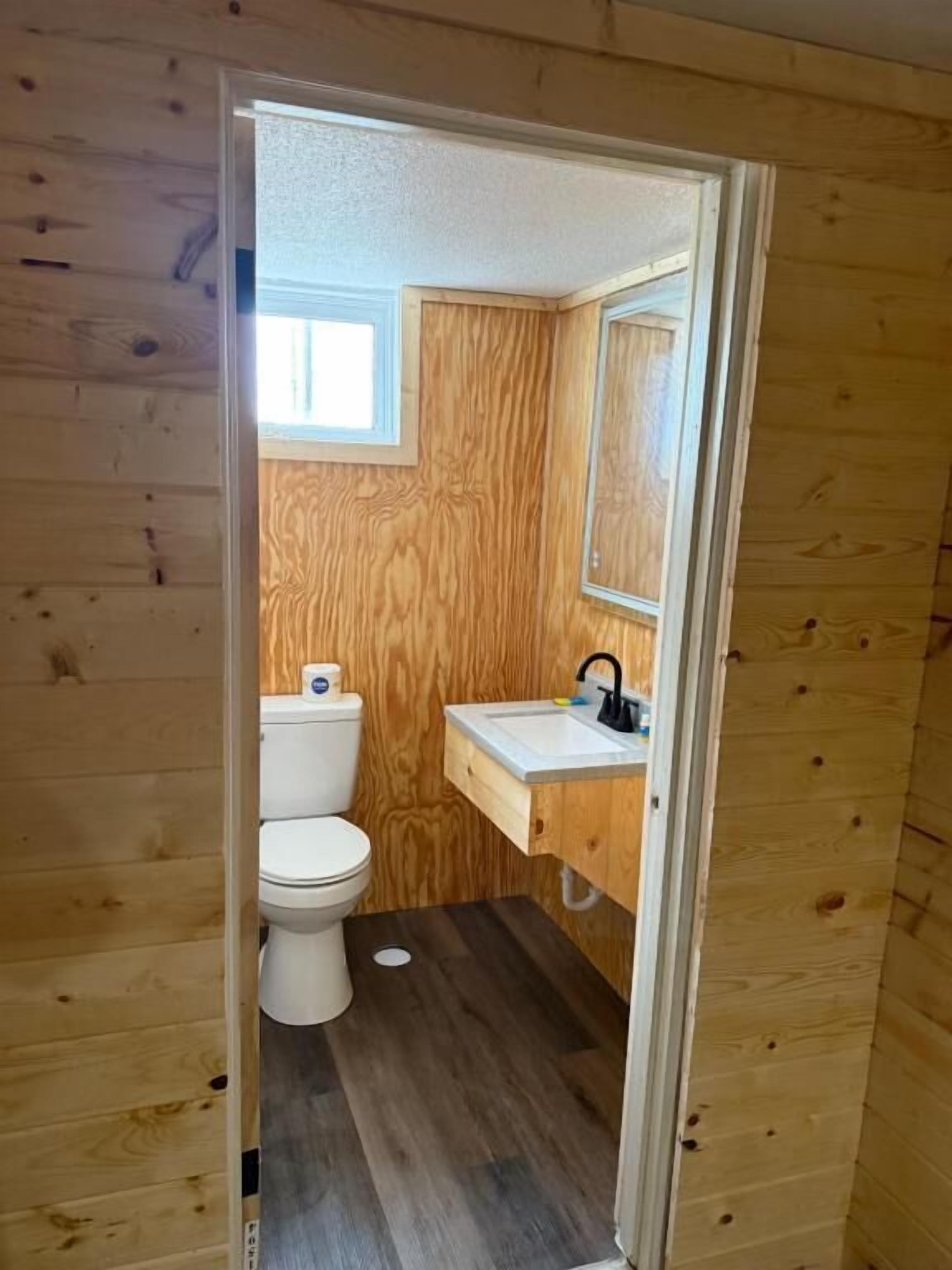 Un baño con paneles de madera, un inodoro, un lavamanos y un espejo.