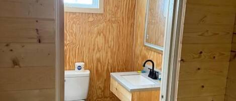 Un baño con paneles de madera, un inodoro, un lavamanos y un espejo.