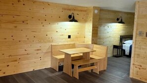 A wooden interior with a central table and benches, wooden walls, and a small table with a chair in the background. - Lake Lawn Inn (Pana)