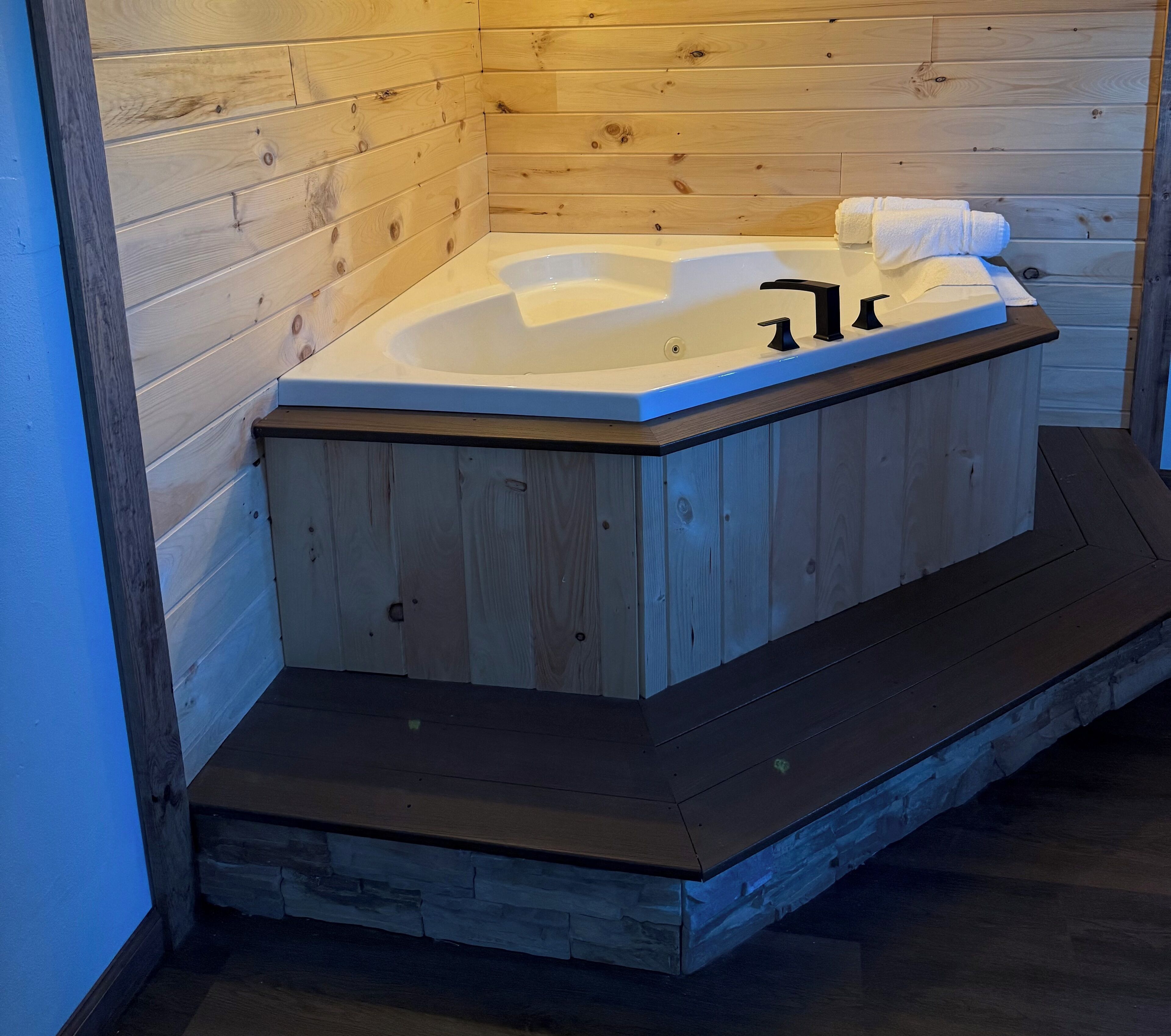 A wooden cabin with a hot tub, wooden walls, and a stone floor.