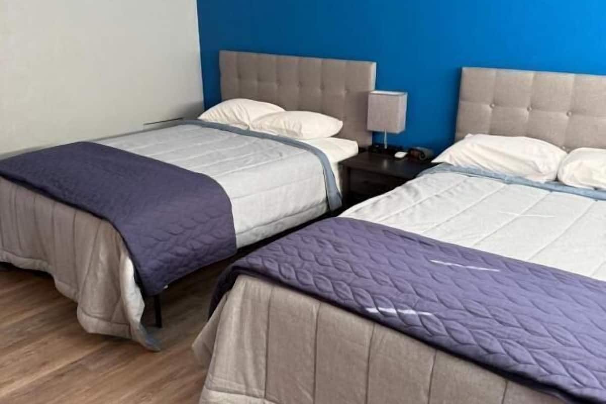 A hotel room with two beds, a nightstand with a lamp, and a blue accent wall.