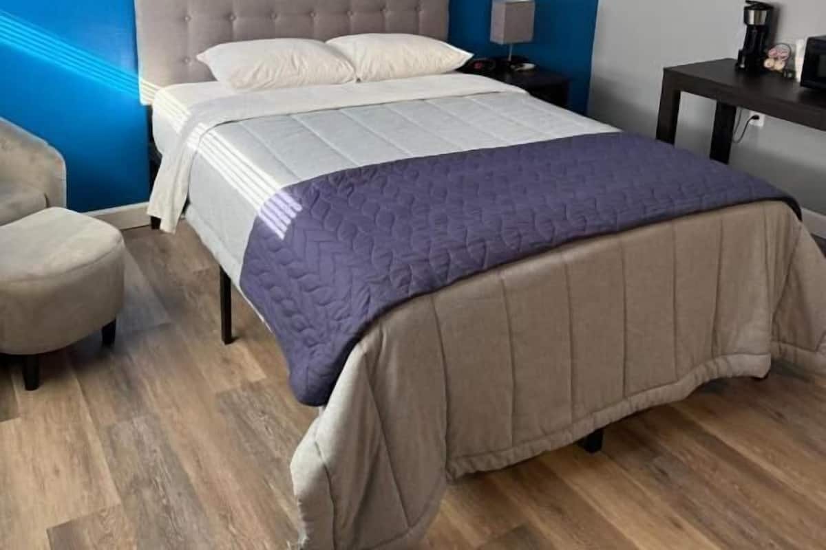 A modern hotel room with a large bed, a bedside table, a chair, and a desk with a coffee maker.
