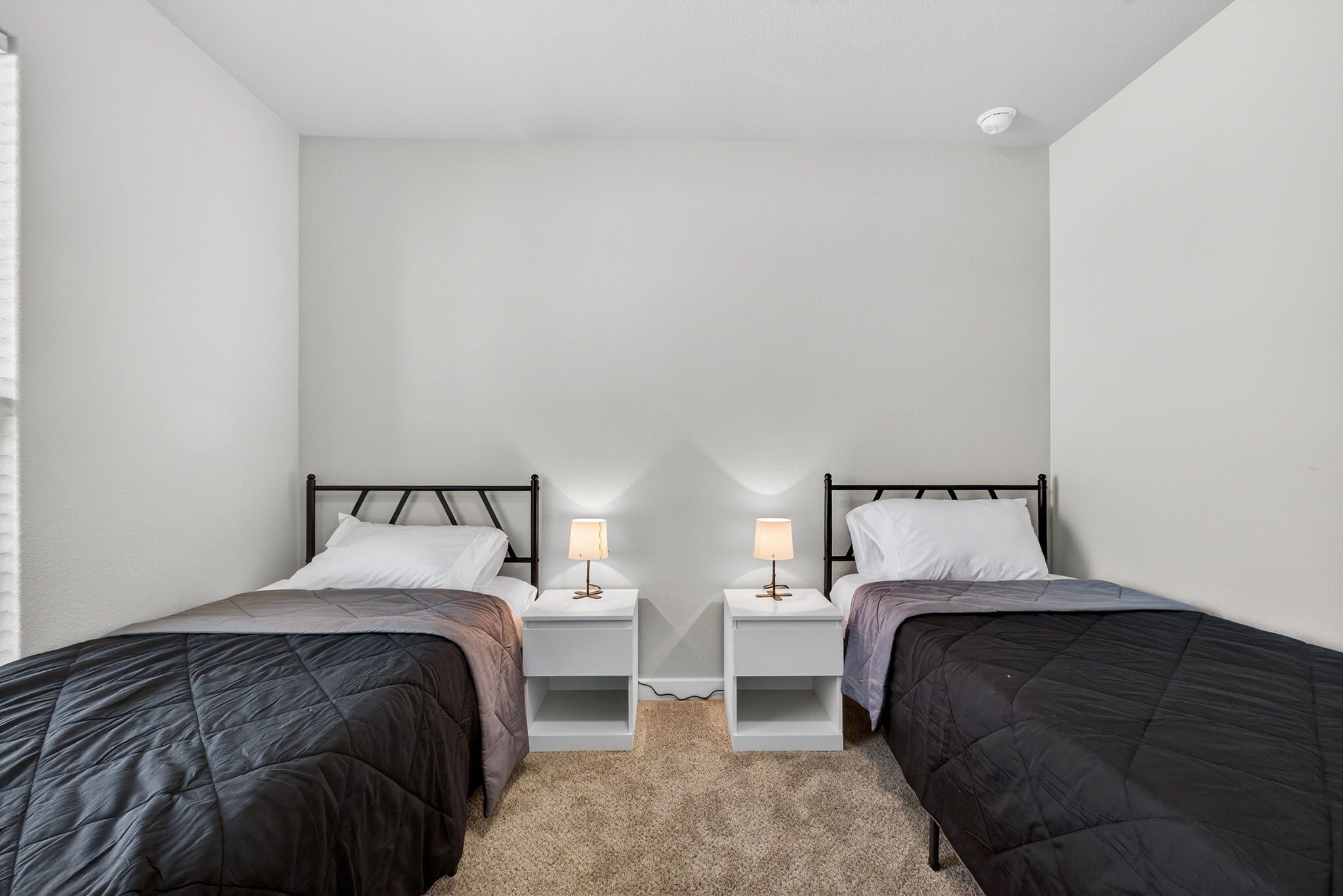 Quarto duplo com duas camas, mesas de cabeceira brancas e abajures.