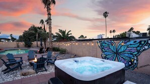 Un patio trasero con jacuzzi, sillas de descanso, piscina y un mural de mariposas.