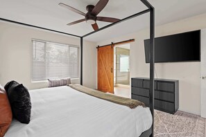 A bedroom with a four-poster bed, a ceiling fan, a TV mounted on the wall, and a sliding door leading to an outdoor area. - Refreshing Pool • Hot Tub • Game Room • Sleeps 11 (Scottsdale)