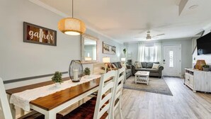 Een ruime woonkamer met een eethoek, een plafondventilator en een groot raam met gordijnen.