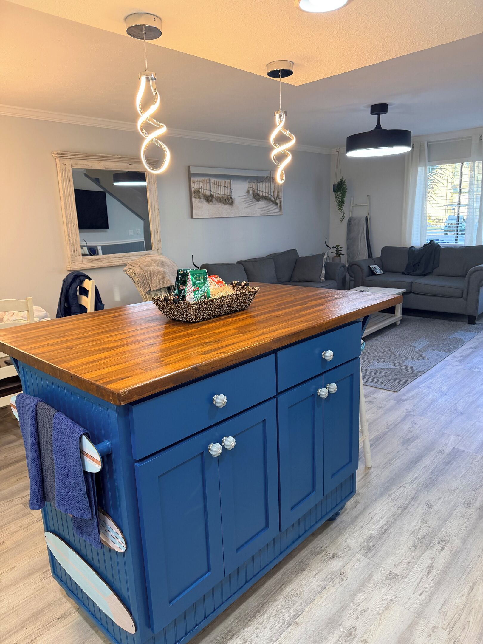 Cocina con un armario azul, encimera de madera y luces colgantes.