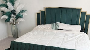 Ein Bett mit einem grünen, gepolsterten Kopfteil und weißer Bettwäsche, ein grünes Sofa und ein farbenfroher Teppich.