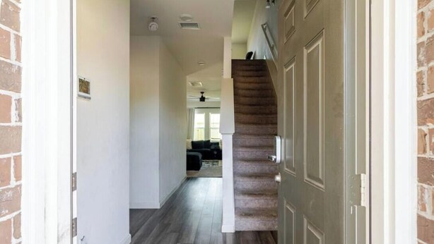 Ein Flur mit einer Treppe, die zu einer Zwischenebene führt, einer Tür rechts und einem Wohnbereich im Hintergrund.