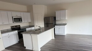 Eine Küche mit weißen Schränken, einer Granit Arbeitsplatte, einem Edelstahlkühlschrank und einer eingebauten Mikrowelle.