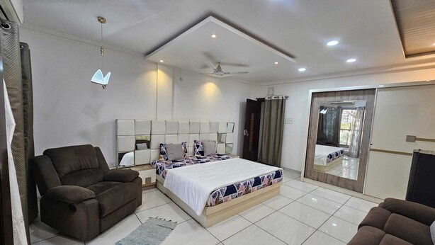 A modern bedroom with a large bed, a sofa, a ceiling fan, and a sliding glass door. - Cozy 1-bedroom fabulous studio in Indore with all amenities. (Indore)