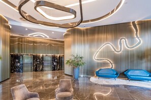 A modern lobby with a marble floor, a reception desk, elevators, and blue seating areas. - Comfortable 2BR City Apartment | Walk Everywhere (Brisbane)
