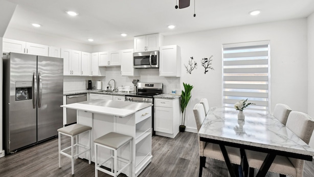 Una cocina moderna con armarios blancos, un refrigerador de acero inoxidable, horno empotrado y un comedor con mesa y sillas de mármol.