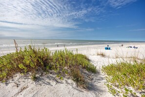 A beach with sand dunes, sparse vegetation, and a clear sky. - Townhouse Pool Across from Beach (Indian Rocks Beach)