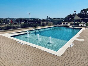 Ein rechteckiger Pool mit drei Wasserstrahlen, umgeben von einer Ziegelterrasse.