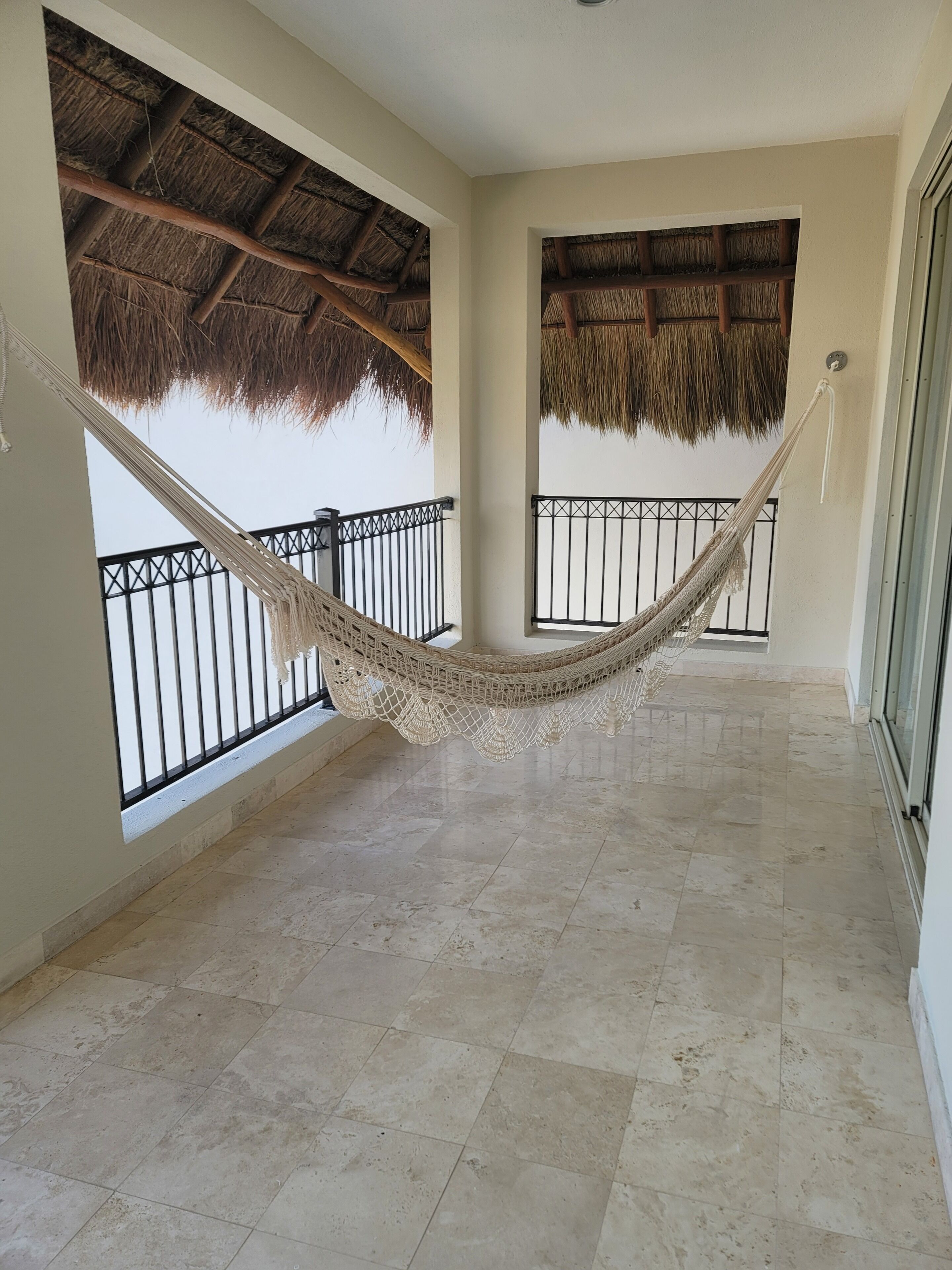 A spacious balcony with a hammock, tiled flooring, and thatched roof ceilings.