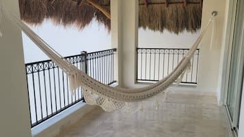 A spacious balcony with a hammock, tiled flooring, and thatched roof ceilings.
